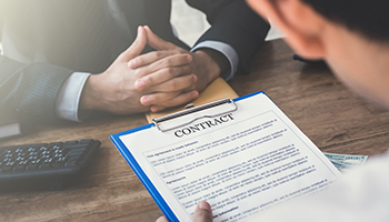 Two businesspeople review and discuss a contract on a clipboard at a desk.